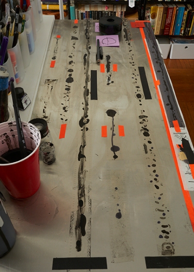 A long animation cel is spread out on a desk, with black ink painted on in blotchy patterns