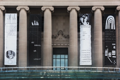 Long vertical black-and-white banners with images and text hang between columns in front of a museum's entrance