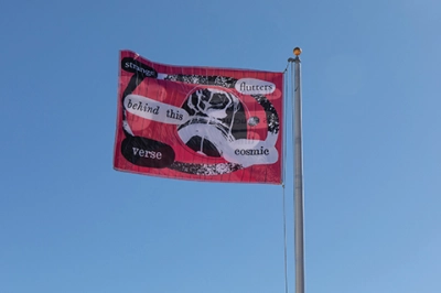 A red flag with black and white art and lettering waves against a clear blue sky