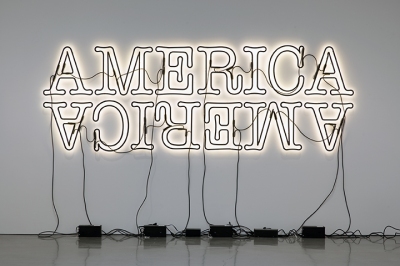 Two neon signs reading America (the bottom one is upside down), installed with the bulbs facing the wall so they create a halo of light around the black lettering