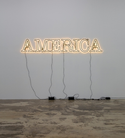 A neon sign reading America hangs on a white wall