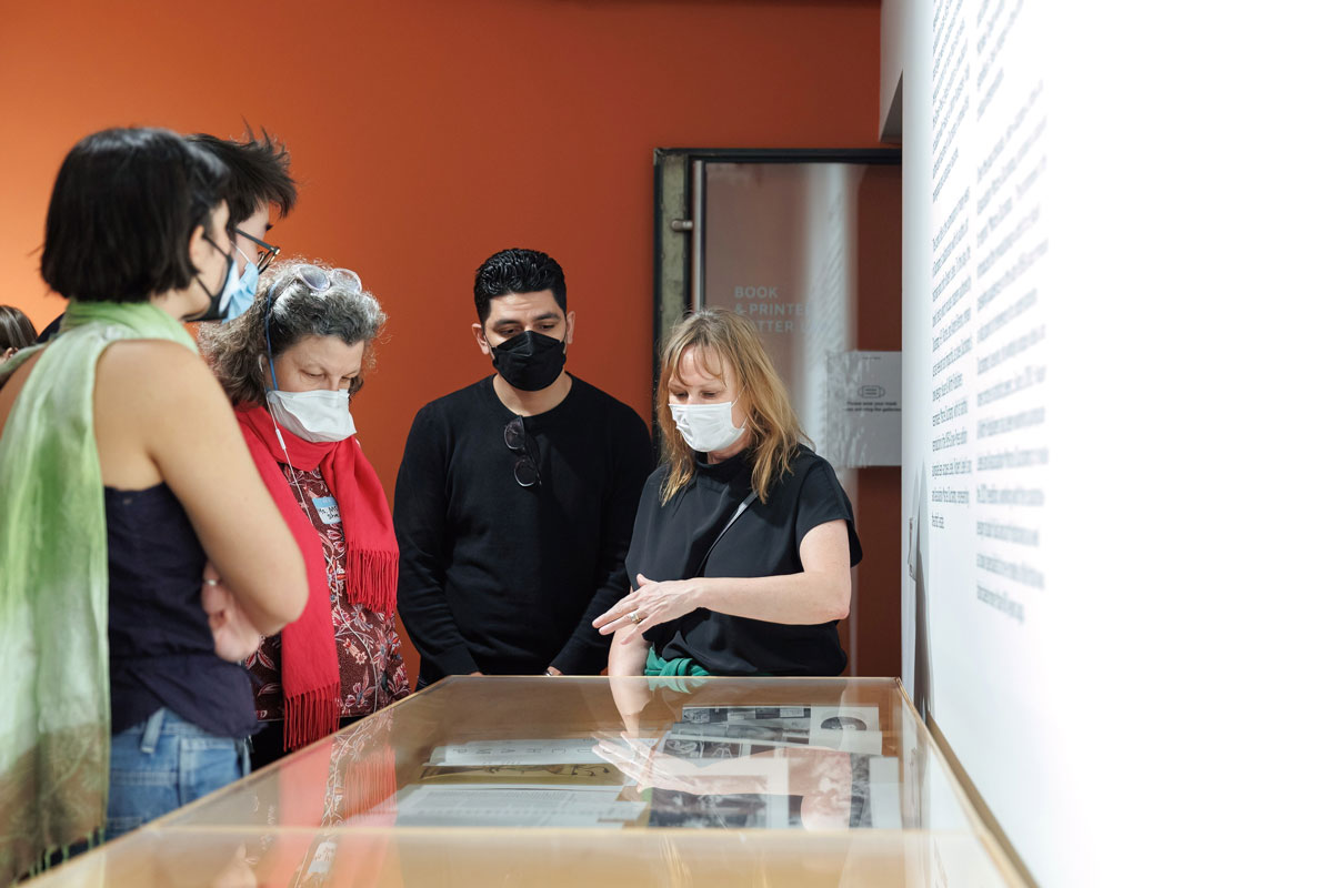 Students and teachers on a tour of an art gallery looking at documents in a vitrine.