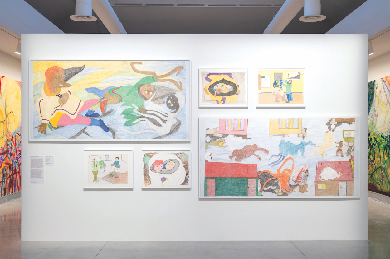 Within a gallery, a grouping of drawings are hung salon-style on a wall. They depict colorful scenes featuring human-creature hybrids.