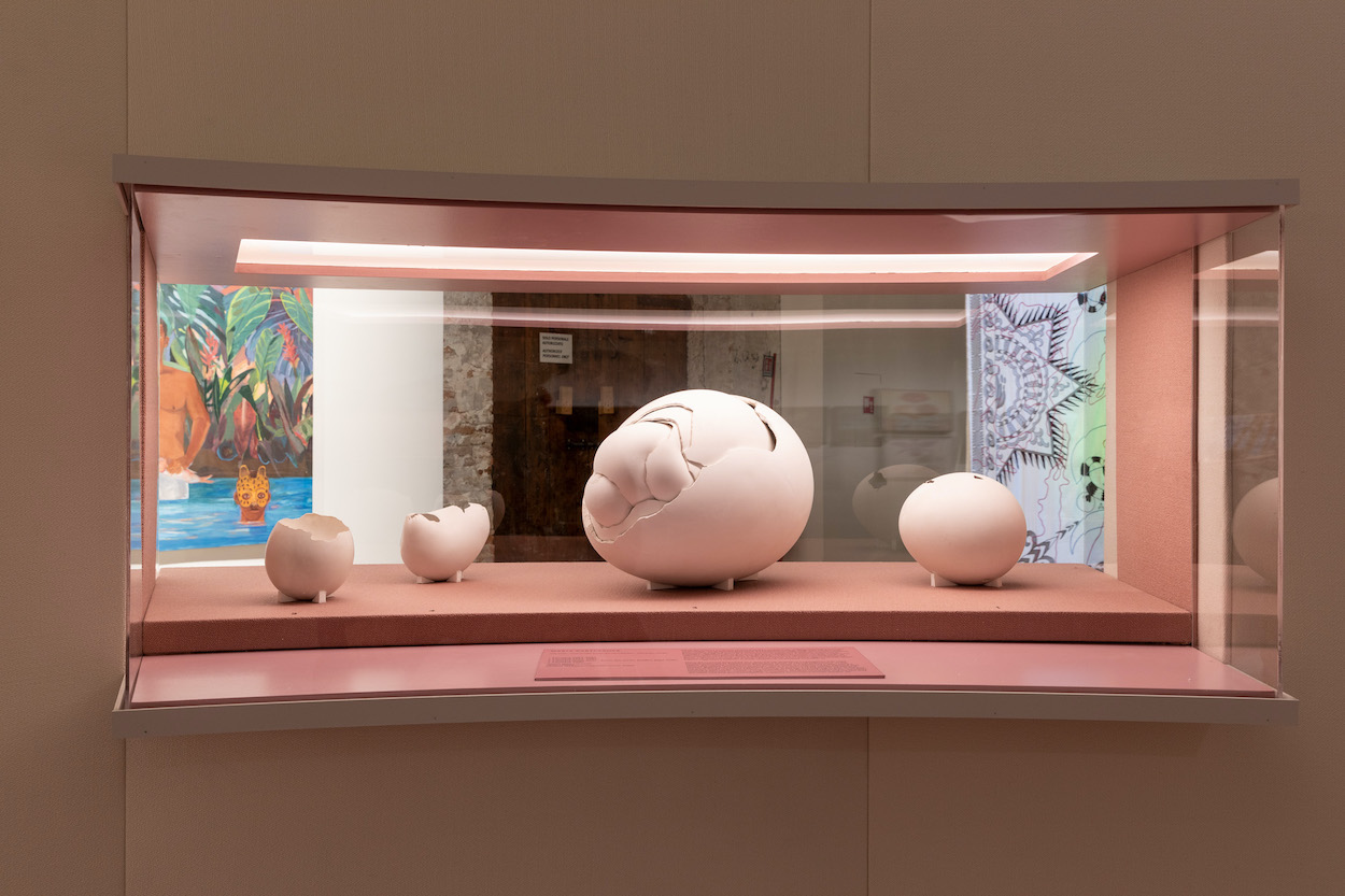 Within a glass display case, a set of sculptures resemble eggs partly cracked open.