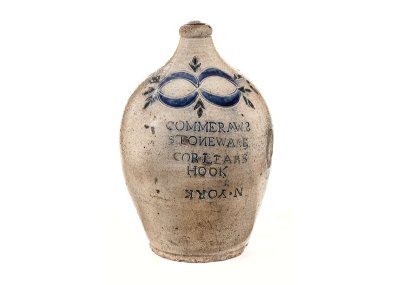 A ceramic jug that a muddy white with blue stamp details and lettering on it. 